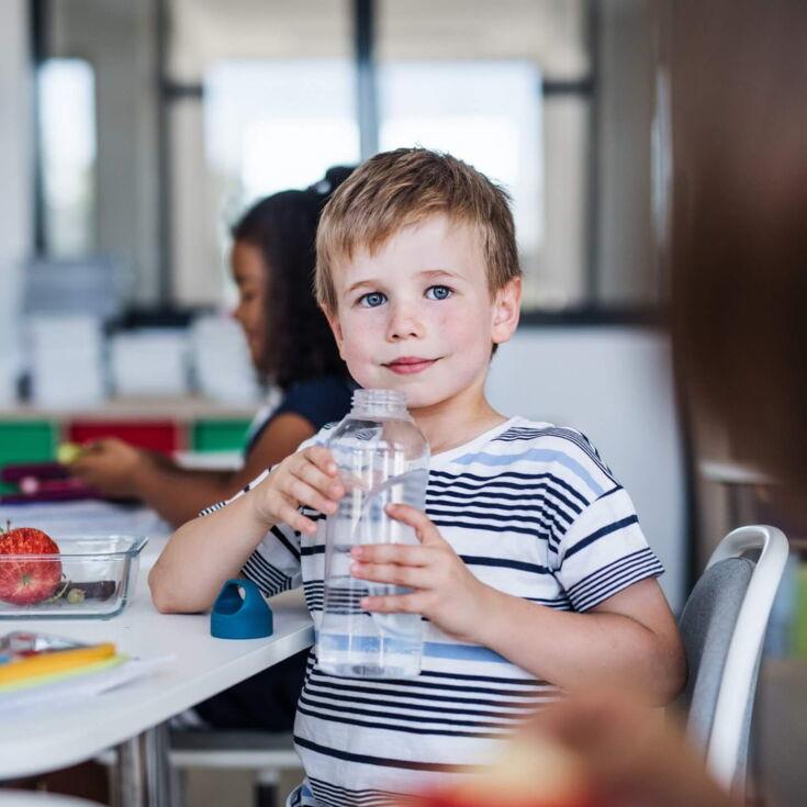 Kleine Junge trinkt Wasser aus Flasche in der Schule